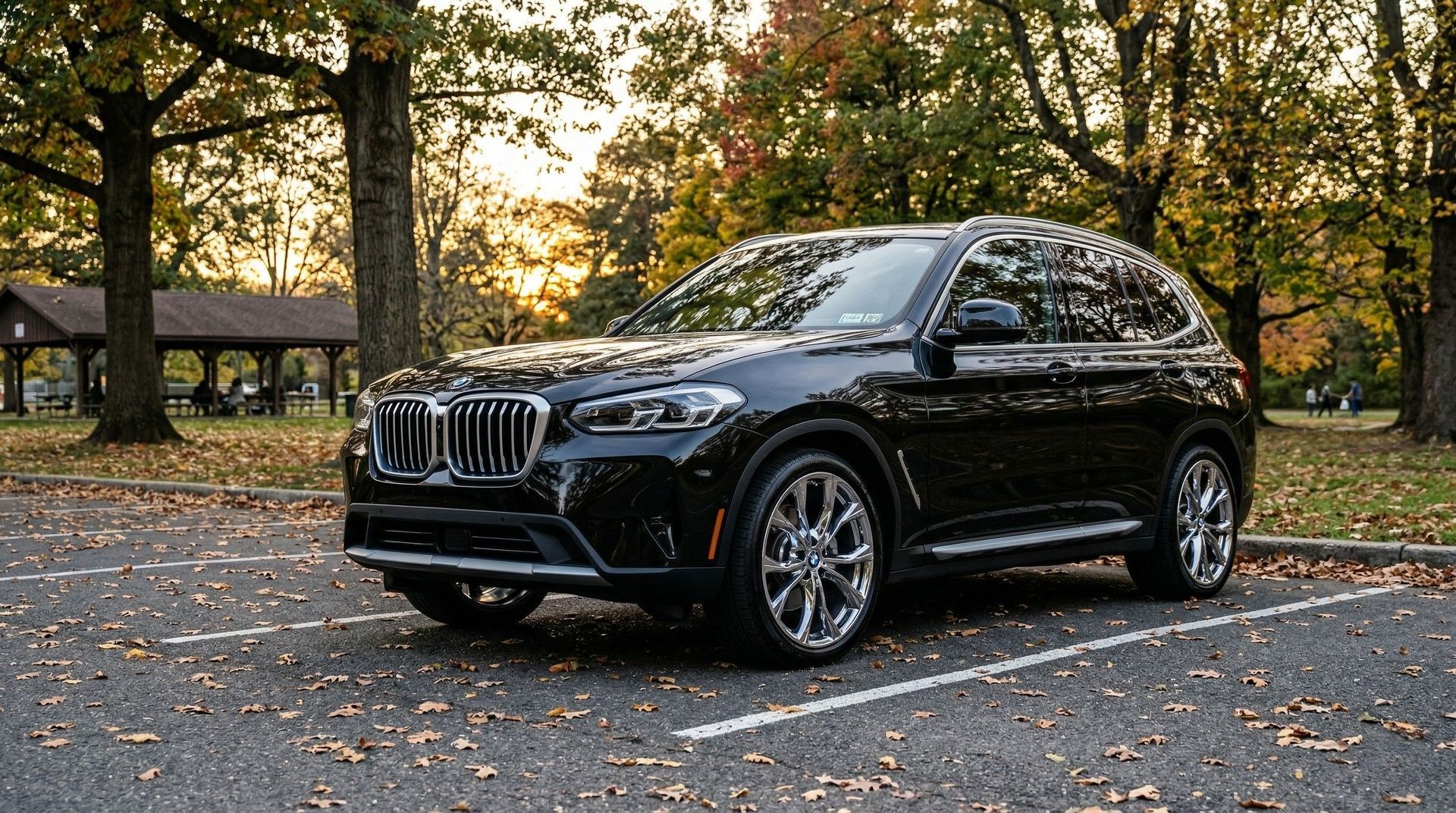 A black BMW SUV parked in a paved lot surrounded by trees with autumn foliage under warm sunlight.