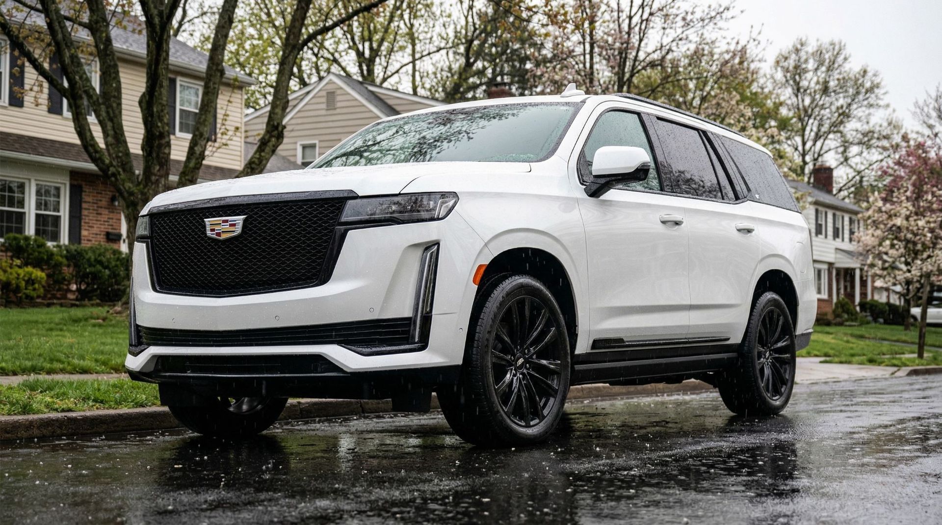 A white Cadillac Escalade parked on a suburban street in front of houses with trees in the background.