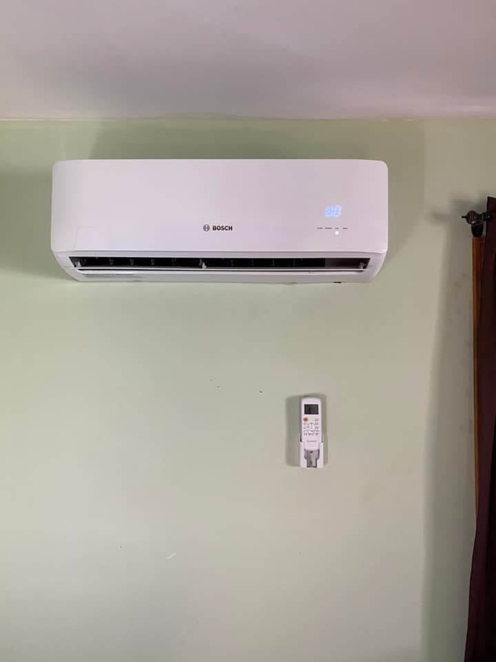 A white air conditioner is hanging on a green wall next to a remote control.