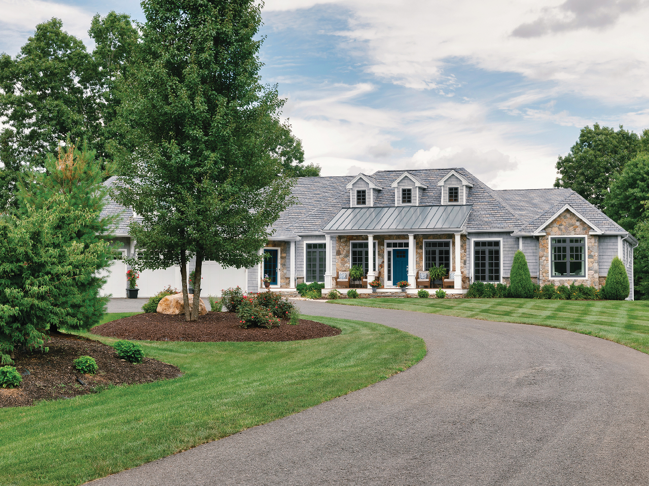 A large white house with a gray roof is sitting on top of a lush green field.