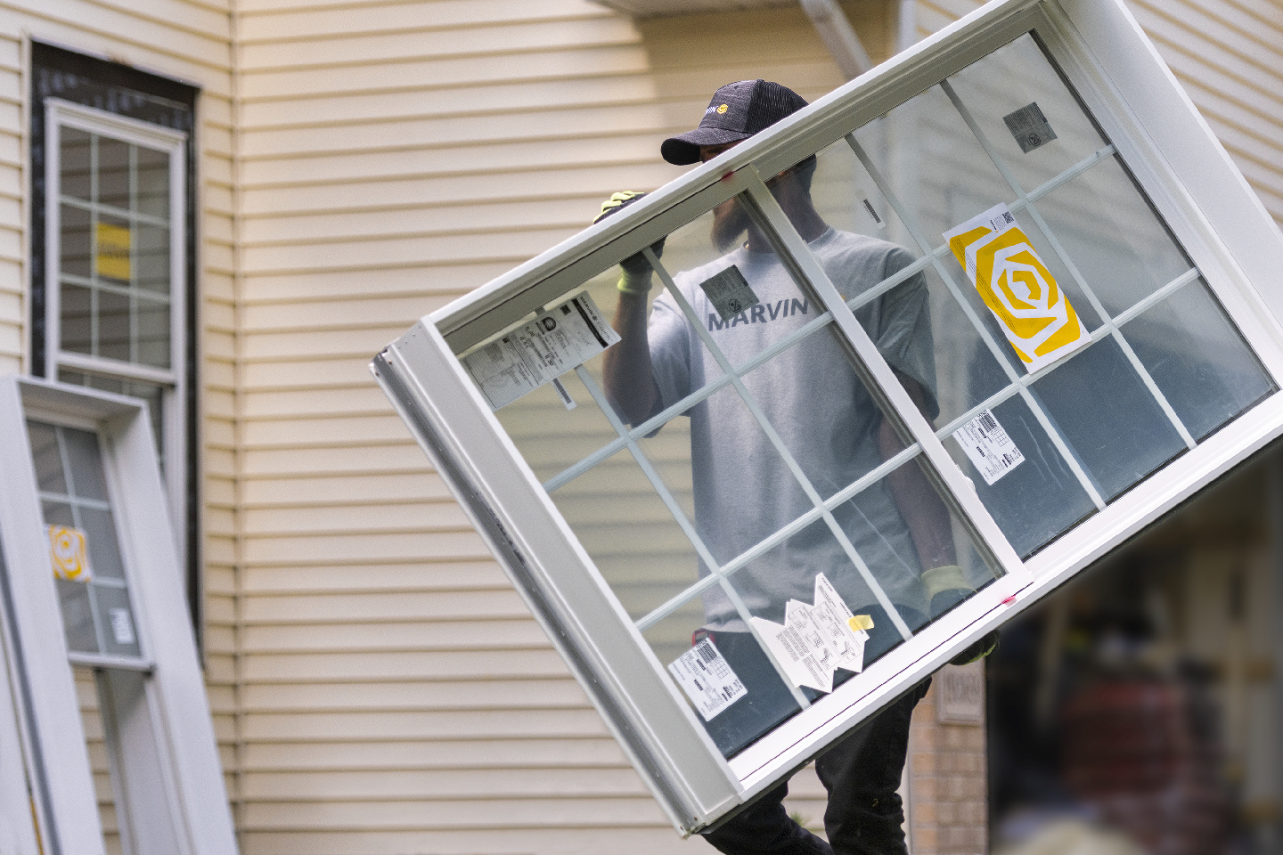 A man is carrying a window in front of a house.