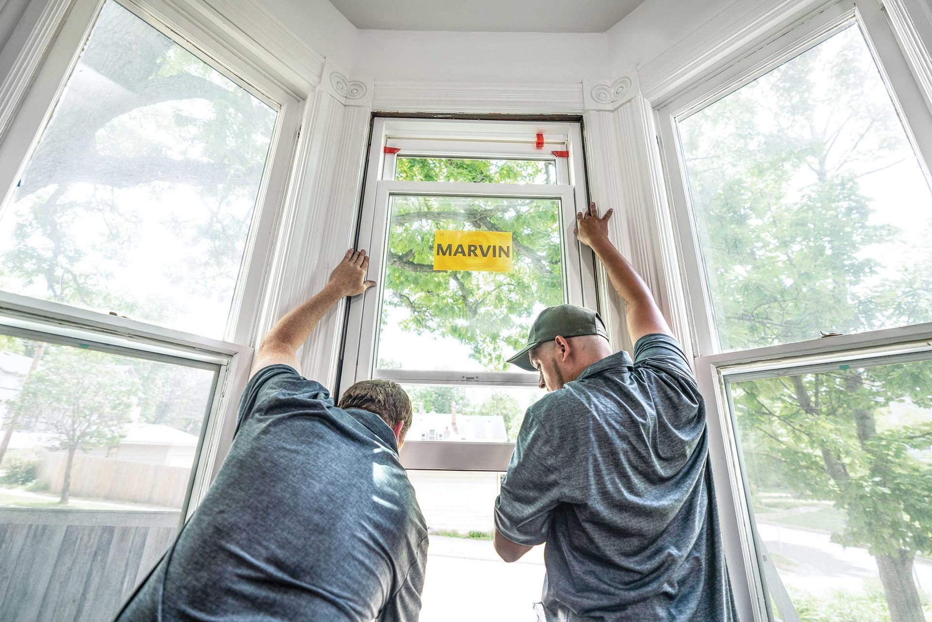 Two men are installing a window in a bay window.