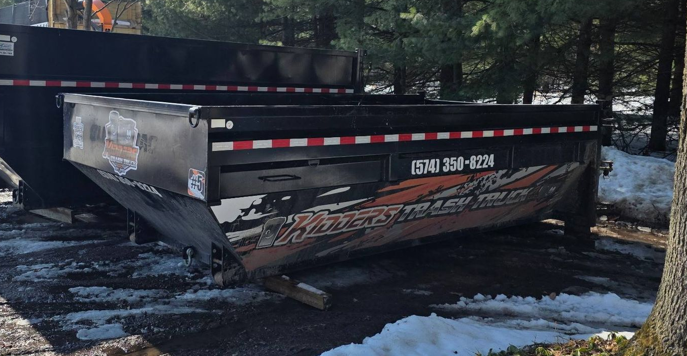 Black Kidder's Trash 14 yard dumpster rental trailer on a snowy roadside in the woods