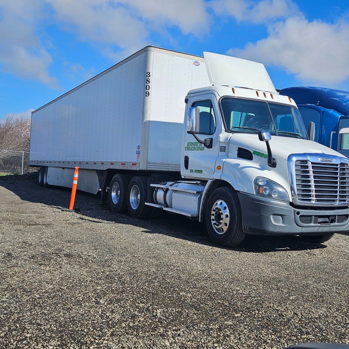 A white semi truck is parked in a gravel lot