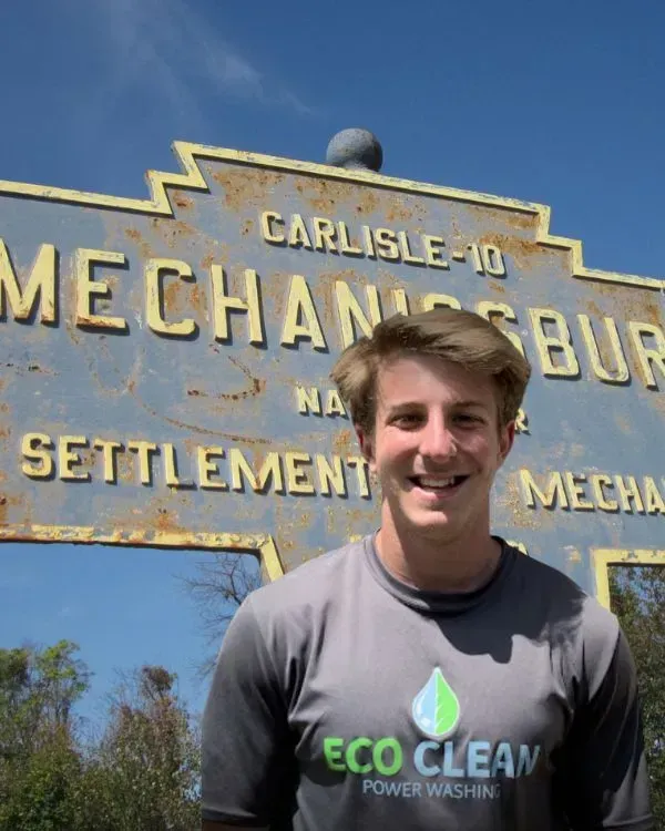 a man wearing an eco clean shirt stands in front of a sign