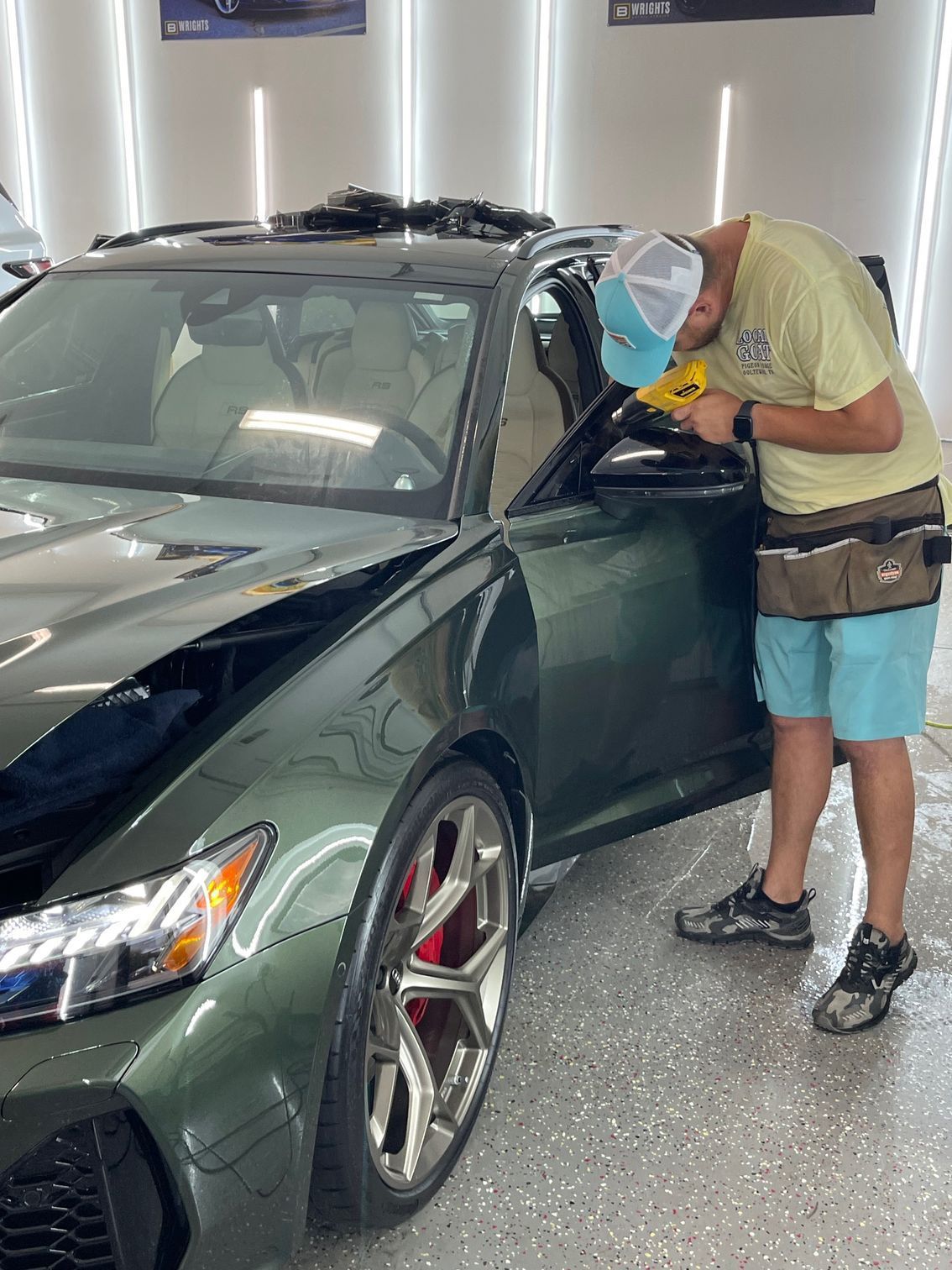 Person applying tint to a black car window in a garage.