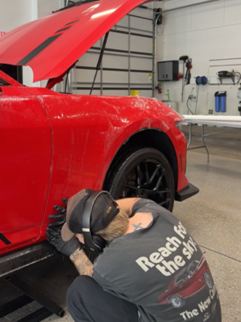 A person working on a red car with the hood up in a garage.