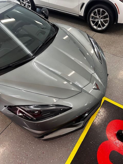 Silver sports car parked indoors, angled view of front. Yellow & black floor marker in view. White SUV in the background.