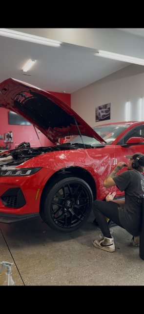 Water droplets beading on a dark, glossy car surface, reflecting light.