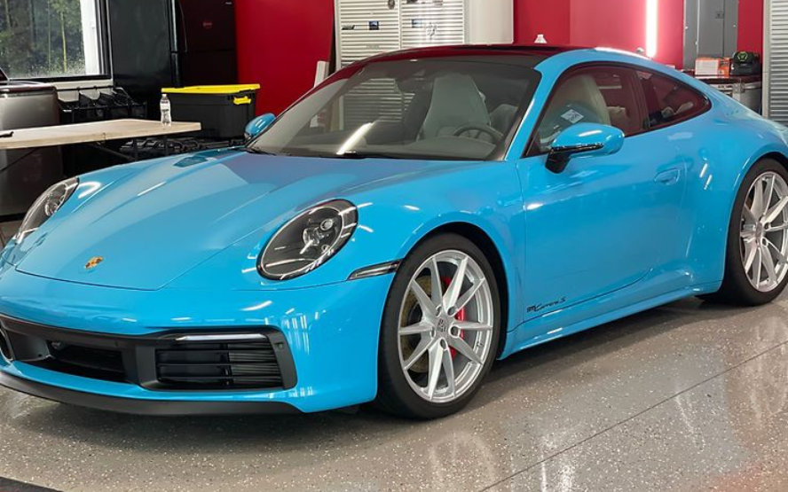 Bright blue Porsche 911 coupe with silver wheels parked indoors.