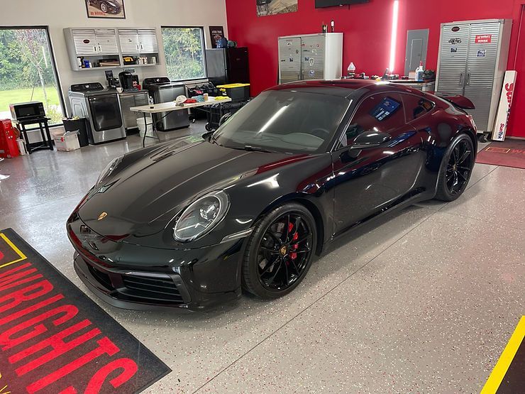 Black Porsche 911 sports car in a garage with red accents and a patterned floor.