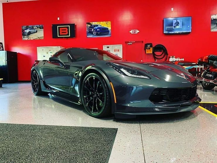 Gray sports car parked inside a building with red walls and artwork.