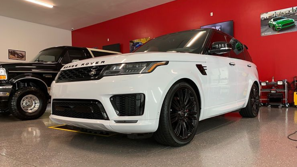 White Range Rover Sport SUV with black rims parked in a garage with red and white walls.