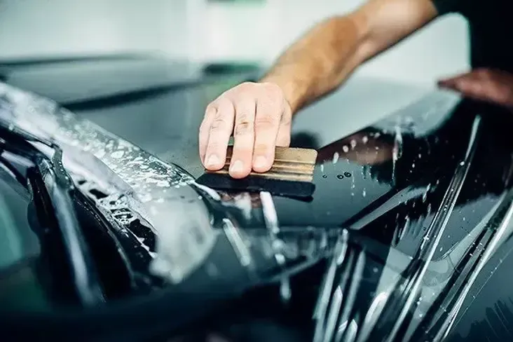 Hand smoothing film onto a car's surface with a squeegee.