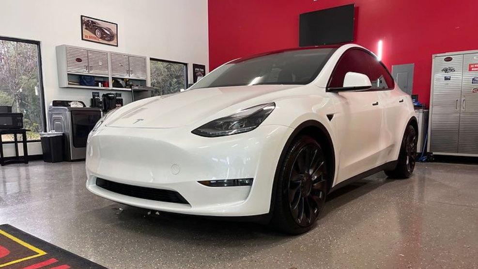 White Tesla Model Y in a red-walled garage with black wheels.