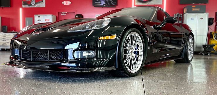 Black Corvette sports car in a red-walled garage, showing off its shiny chrome wheels and sleek design.