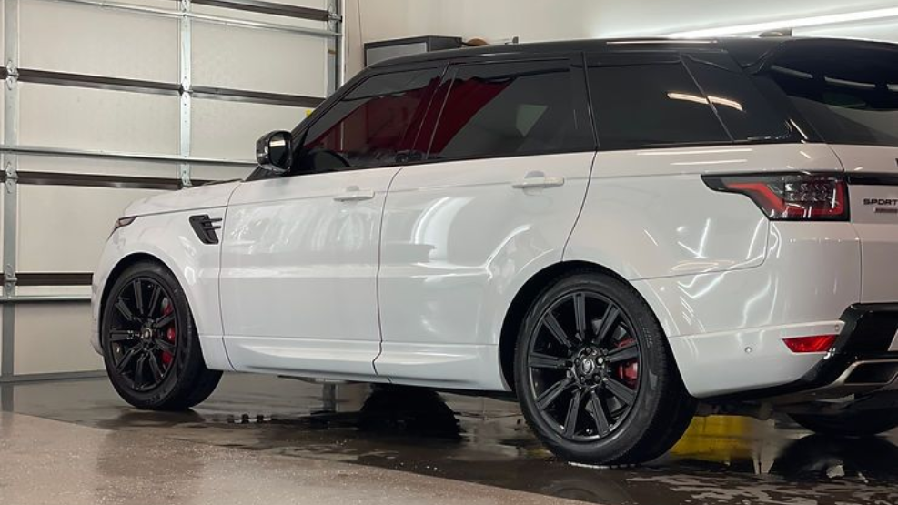 White Range Rover Sport SUV, black wheels, in a car wash bay.