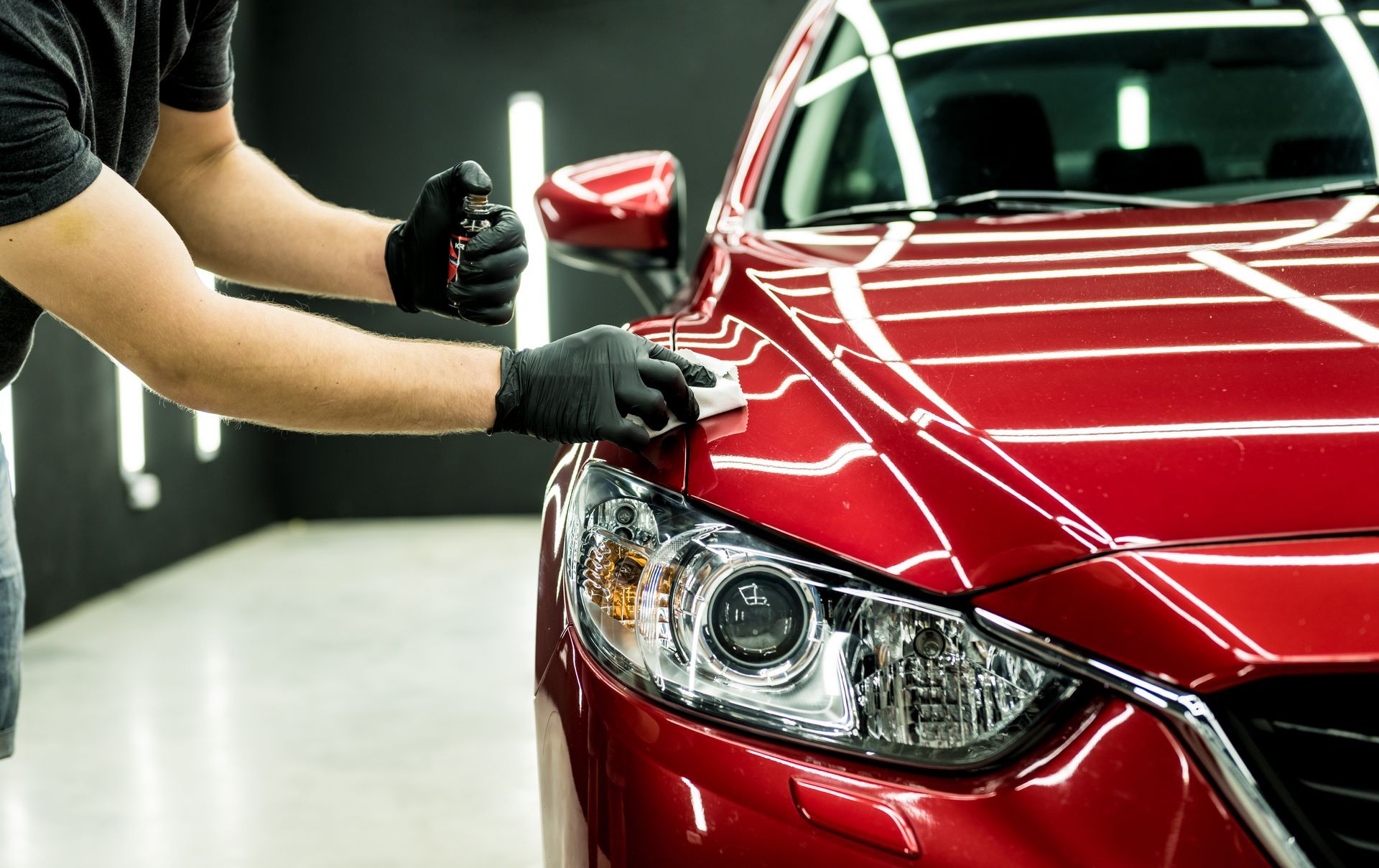 A person in a red hoodie and black pants polishes a black SUV in a garage.