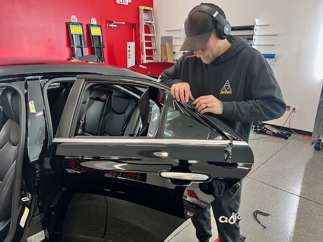 A person in a red hoodie and black pants polishes a black SUV in a garage.