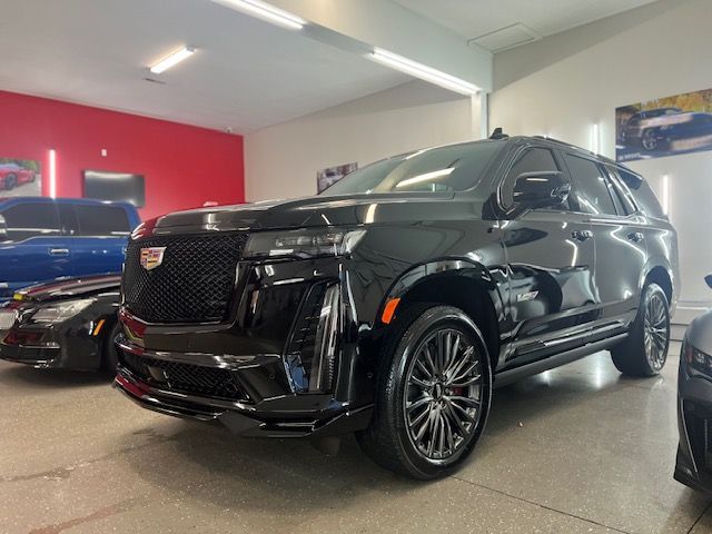 Water droplets beading on a dark, glossy car surface, reflecting light.