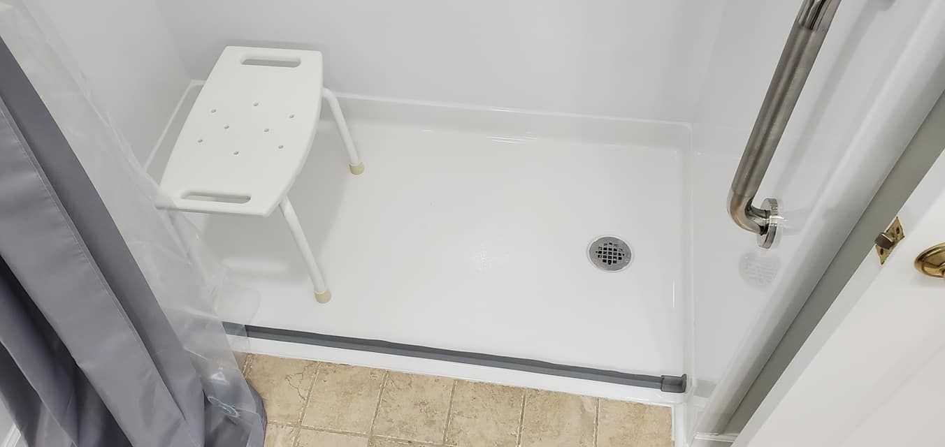 A shower with a stool in it and a drain.
