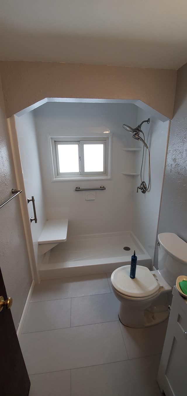 A bathroom with a toilet , shower and window.