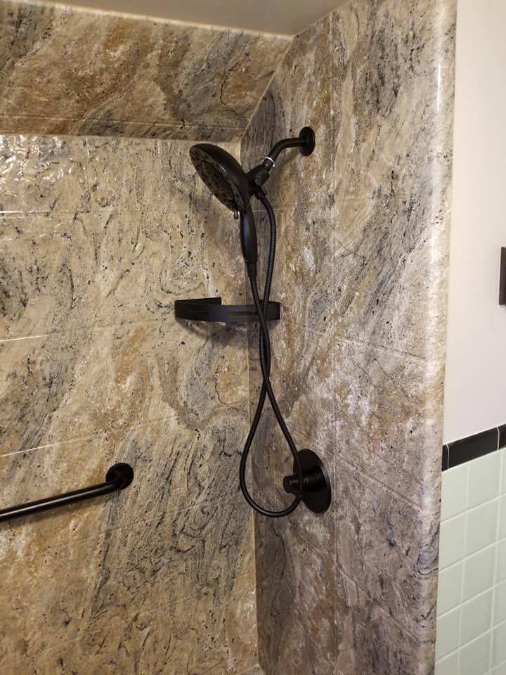 Shower with black fixtures and grab bar against beige and brown tiled walls.