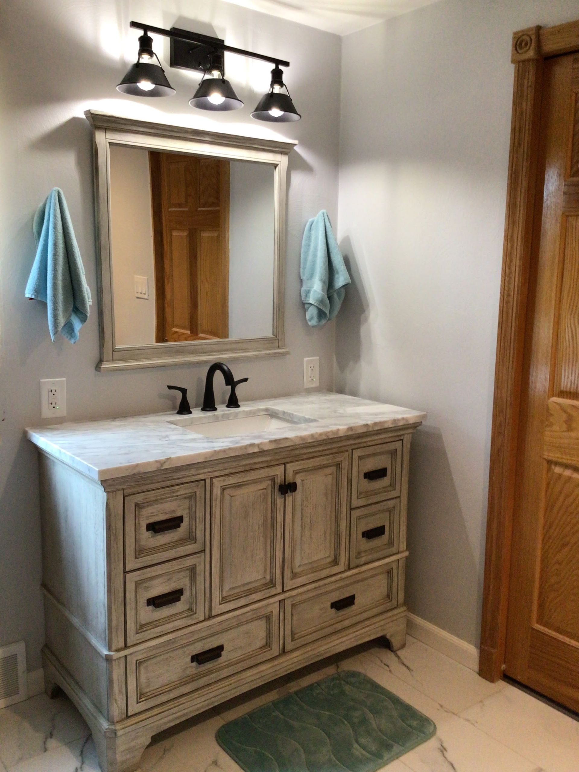 A bathroom with a vanity , sink , mirror and towels hanging on the wall.