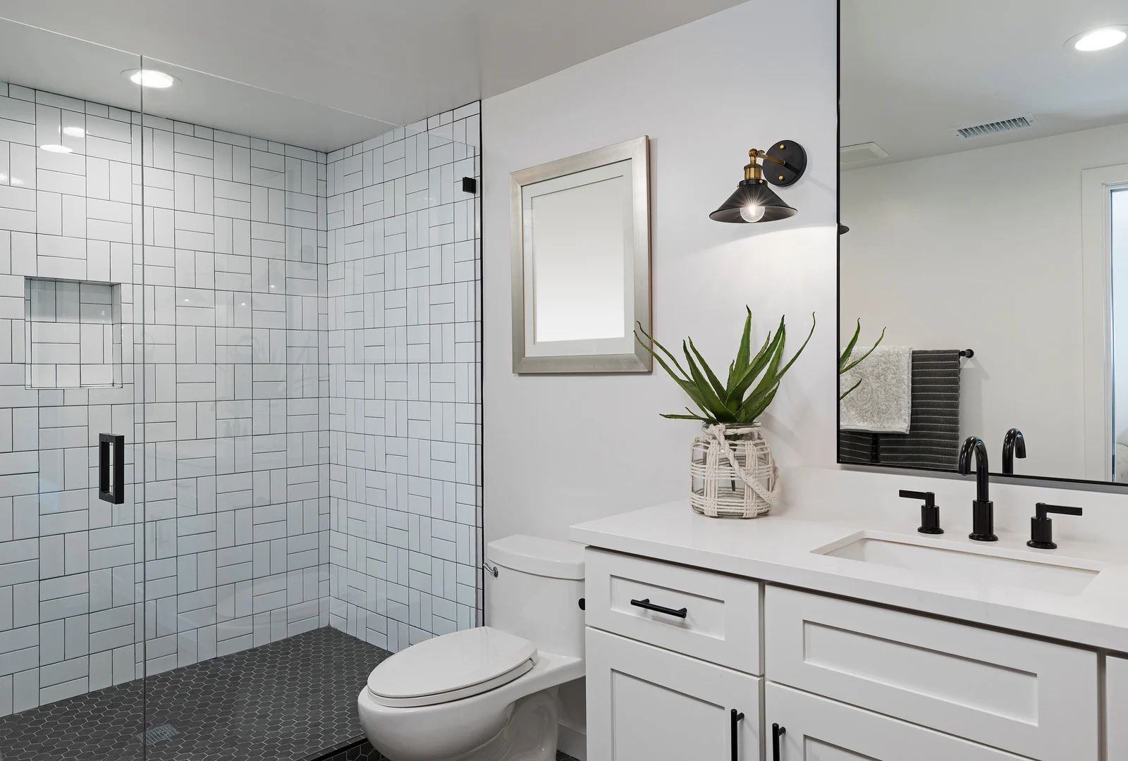 White bathroom with shower, toilet, and vanity. Gray tile shower, white cabinets, black fixtures, and a small mirror.
