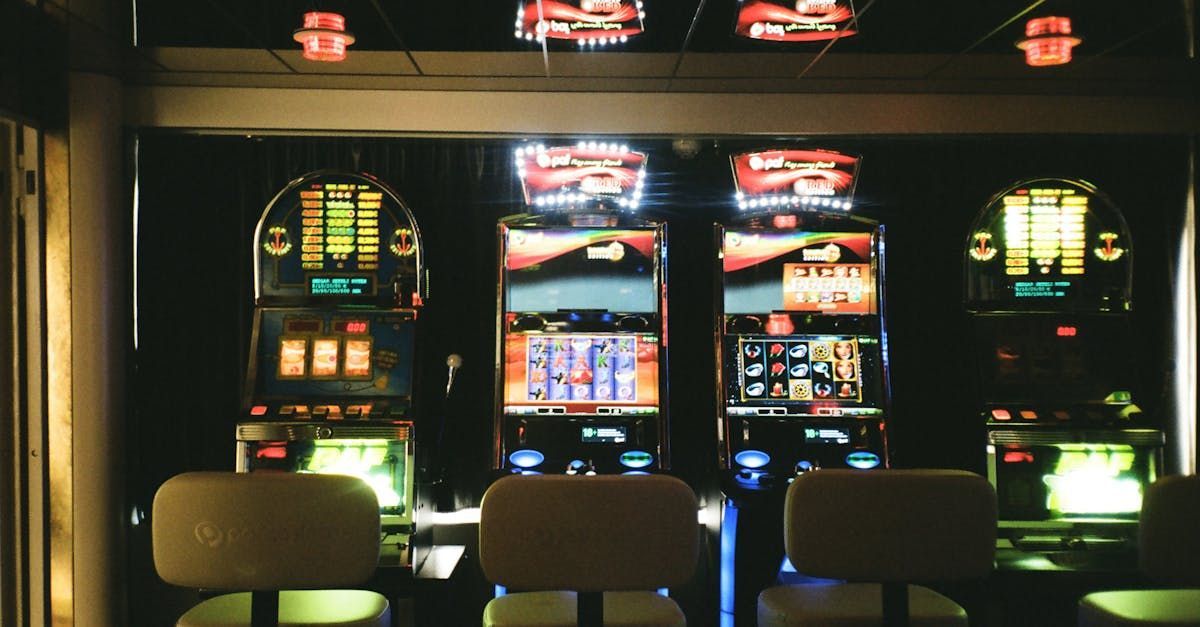 Three slot machines are lined up in a room with chairs.