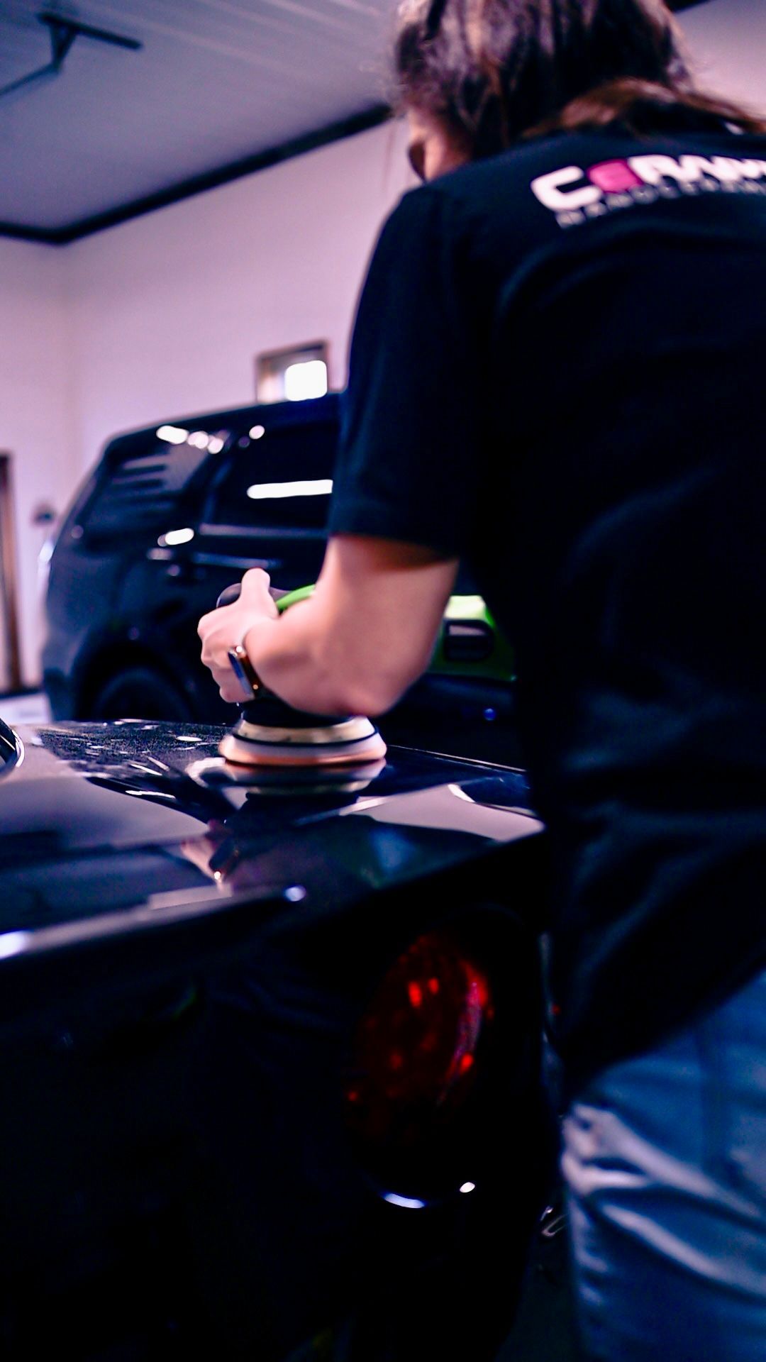 Person using a buffer to polish a black car in a garage or workshop.