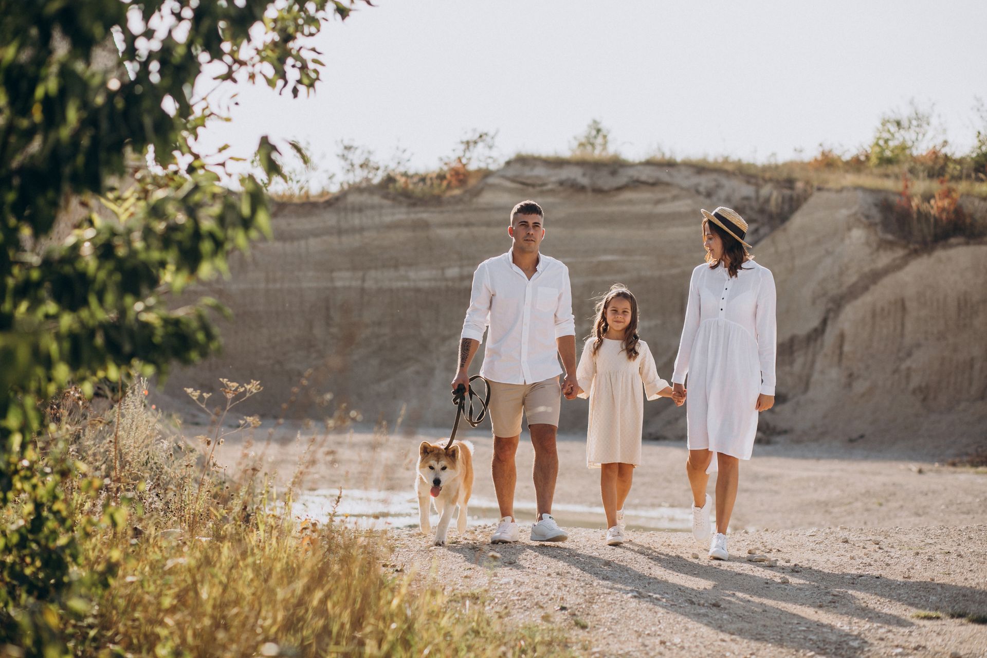 A family is walking a dog on a leash on a dirt road.