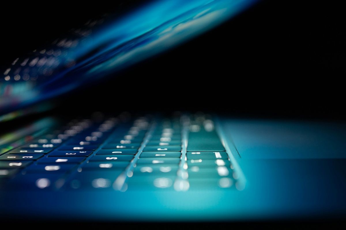 Close-up of a glowing laptop keyboard in blue light, viewed at an angle with the screen above