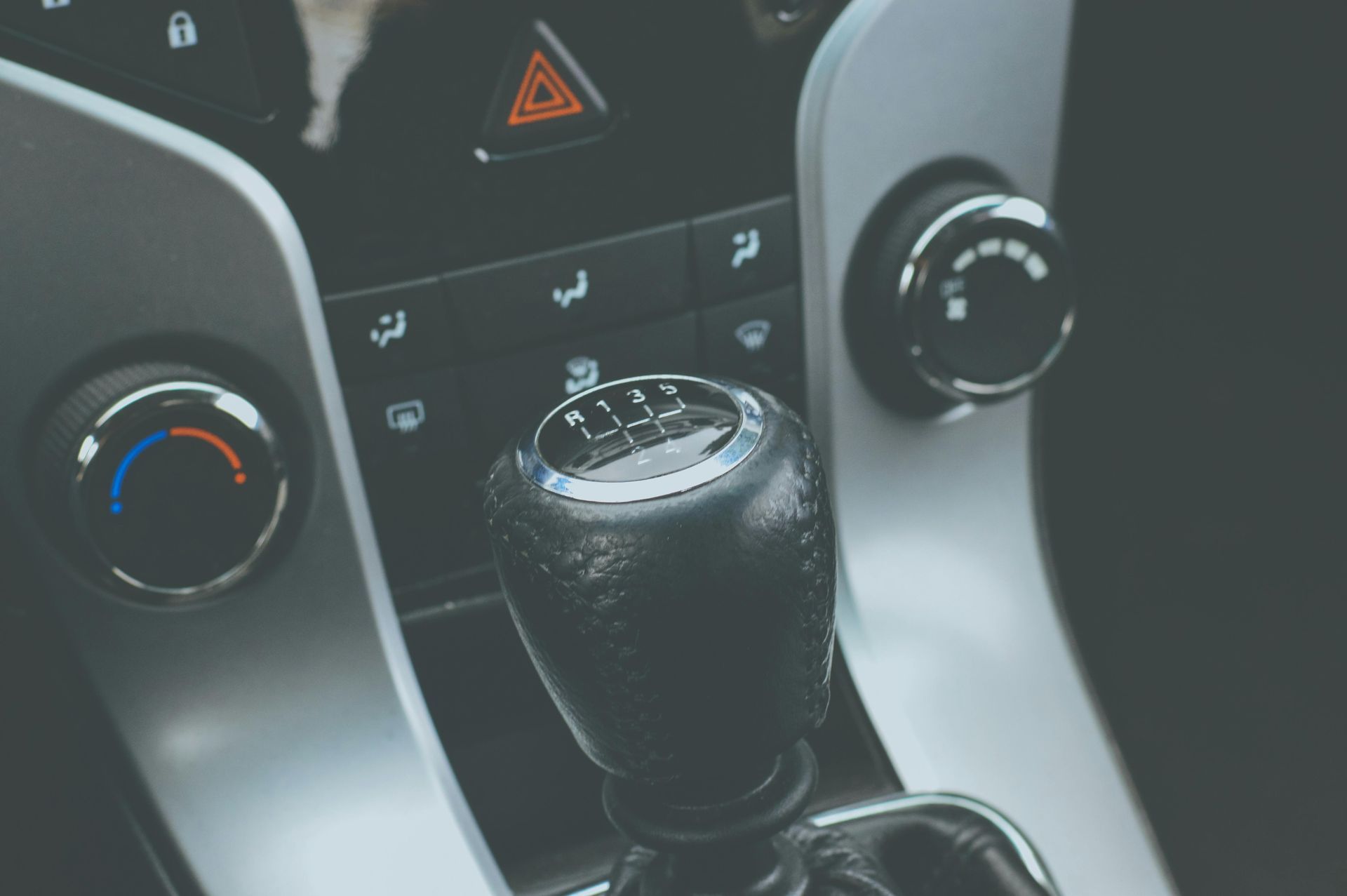 Black gear shift in a car, surrounded by climate control knobs on a dashboard.