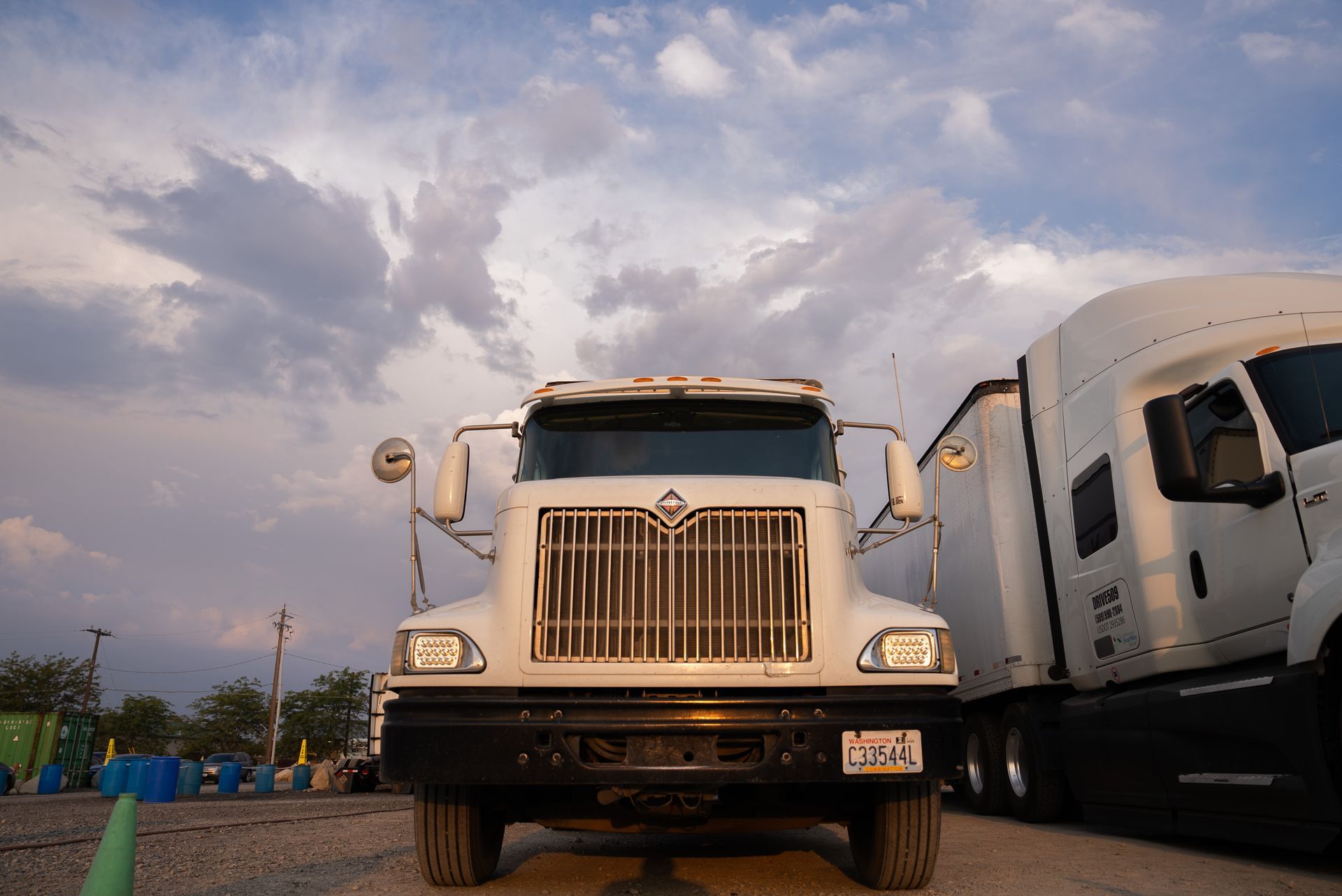 Two white semi-trucks parked side-by-side on a gravel lot under a cloudy sky.