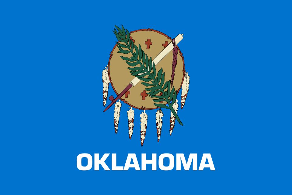 Flag of Oklahoma: sky-blue field with an Osage warrior's shield, peace pipe, and olive branch, and the word Oklahoma in white below.