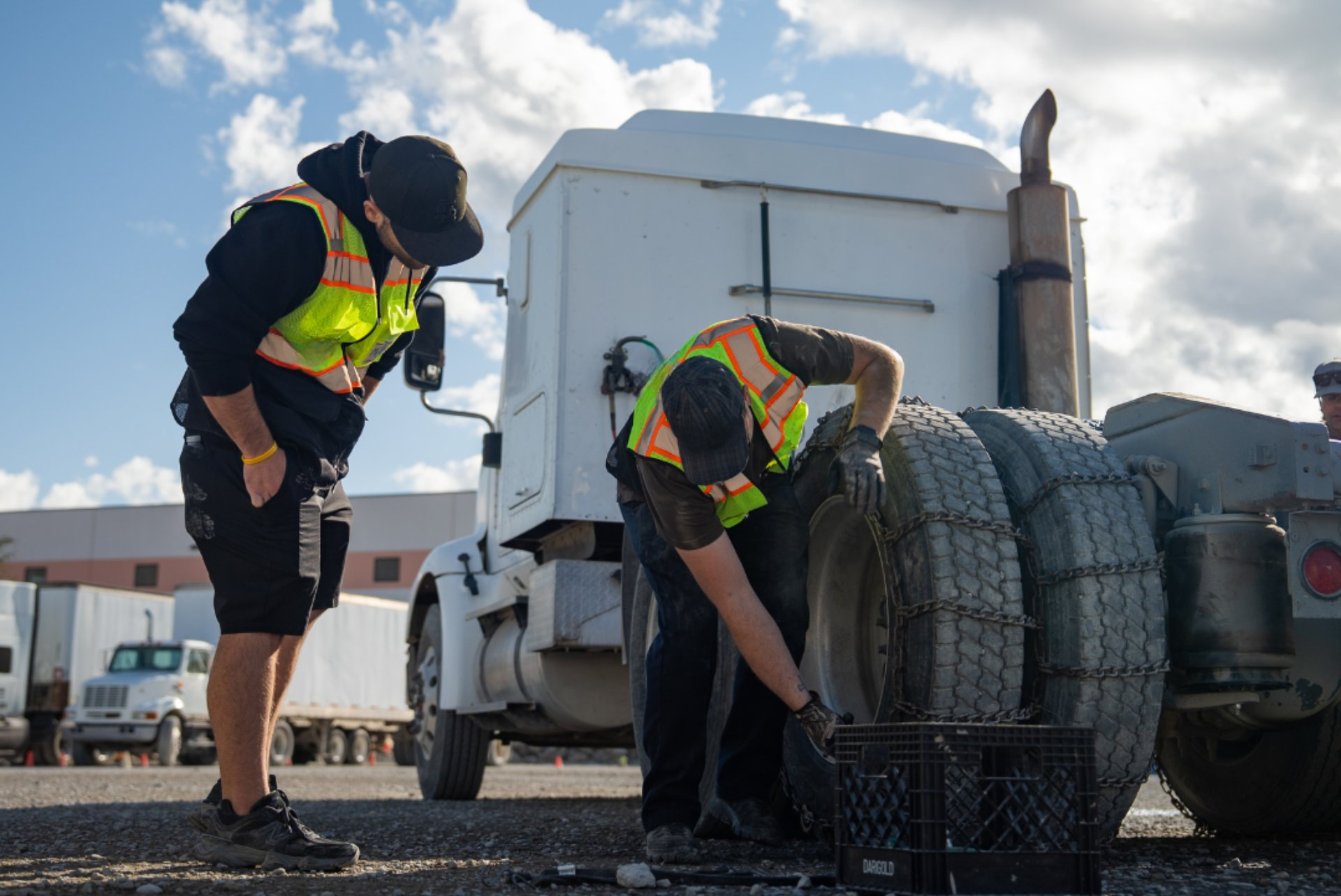 CDL students in safety vests gather for a yard briefing beside a white training truck and cones