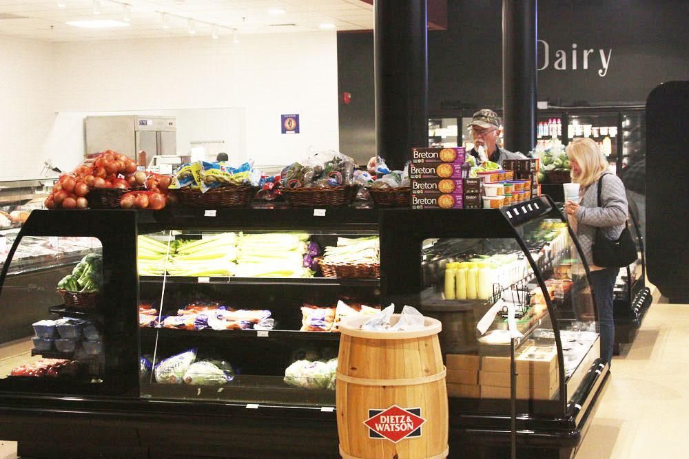 Produce displays in a store featuring shelves of fresh fruits and vegetables with a wooden barrel in the foreground.