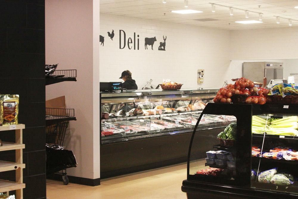 A deli counter in a supermarket with a glass display case of meat and a worker standing behind it.