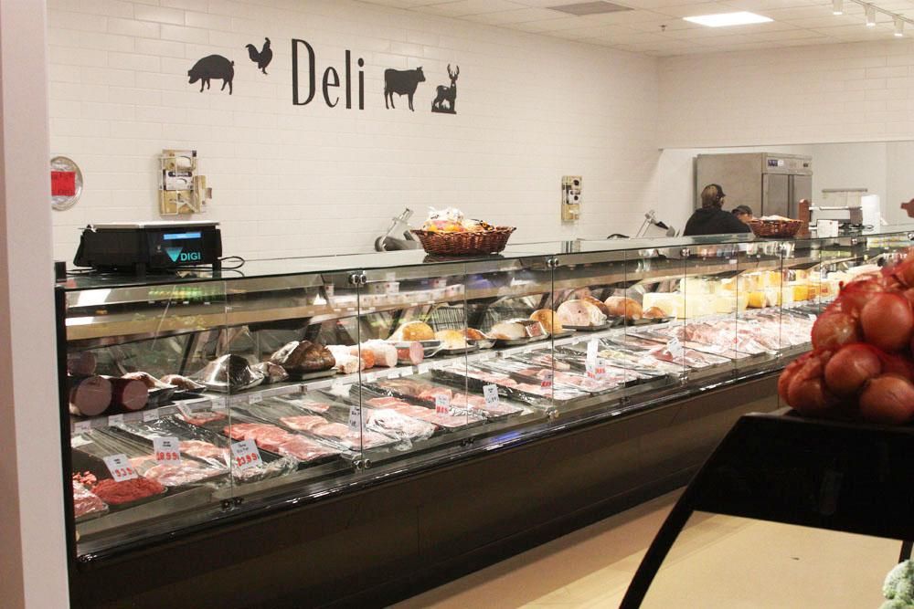 A long deli meat counter in a store, with silhouetted animal icons above the sign and fresh produce in the foreground.