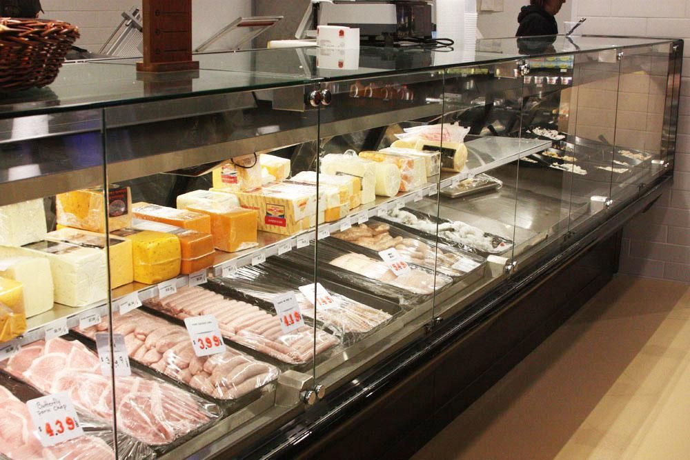A refrigerated glass display case in a store, filled with various cheeses and rows of raw packaged meat.