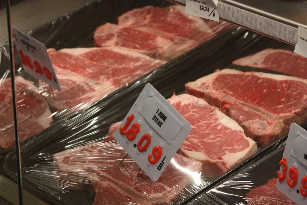 Plastic-wrapped raw T-bone and New York strip steaks displayed in a refrigerated grocery store meat case.