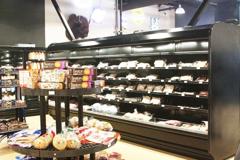 A grocery store aisle featuring a circular display stand of baked goods in front of a long, black refrigerated shelf unit.
