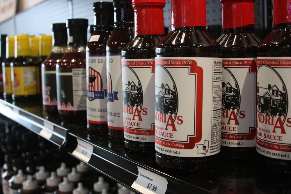Bottles of Doria's barbecue sauce with red caps lined up on a grocery store shelf.