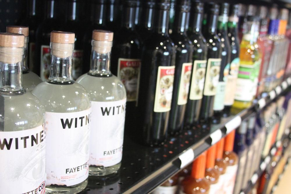 Bottles of Witness spirits and dark liquid on a retail shelf, arranged in rows.