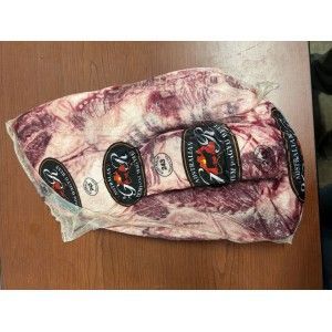 A vacuum-sealed slab of marbled Australian Wagyu beef sits on a brown surface, featuring several brand logo stickers.