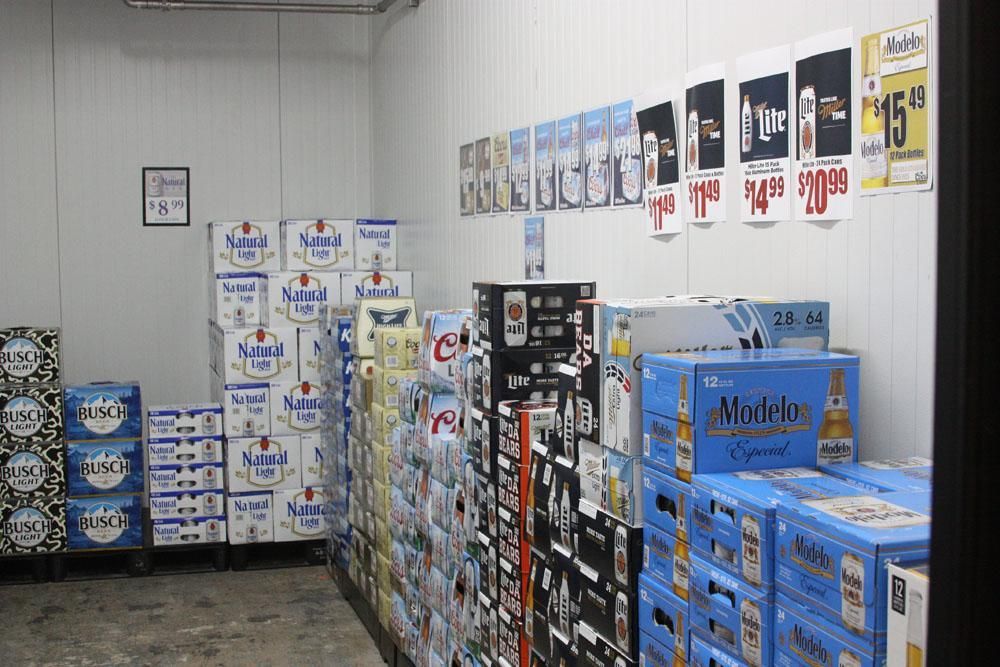 Stacked cases of beer and beverages fill a walk-in cooler, with product signage displayed on the wall above.
