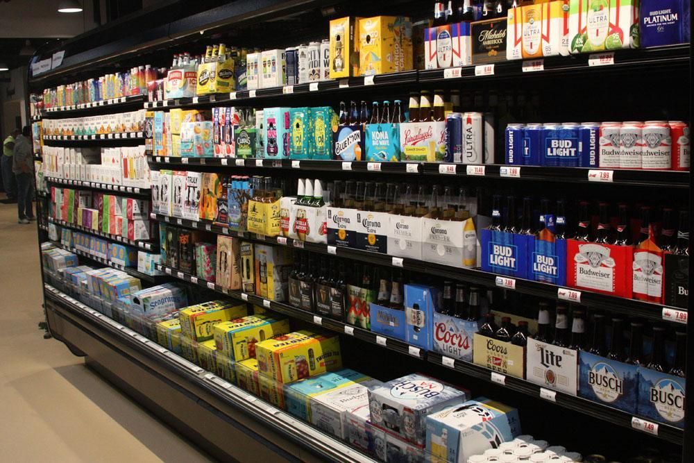 A large, refrigerated store shelf stocked with various brands and packs of beer and alcoholic beverages.