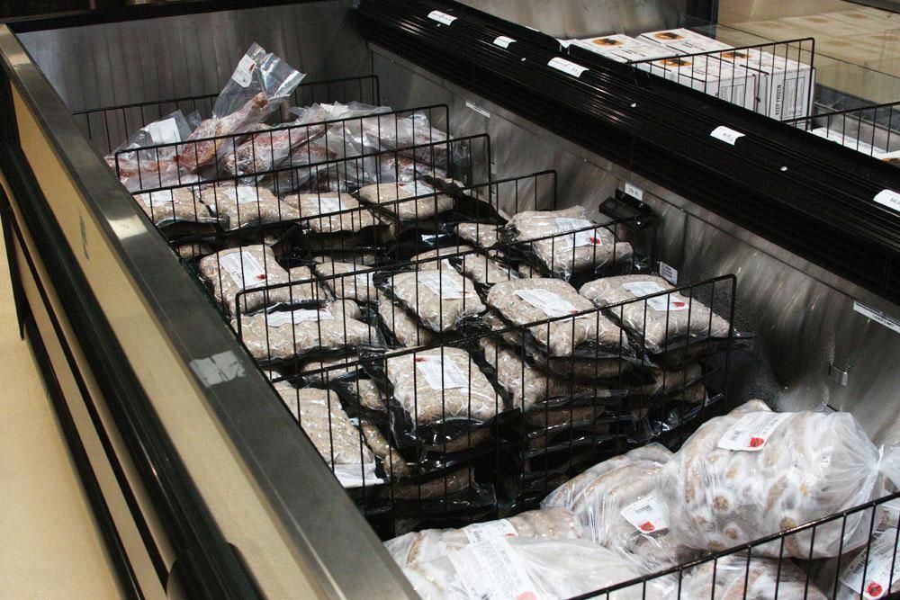 A store freezer display case filled with packages of raw, frozen meat arranged in wire baskets.