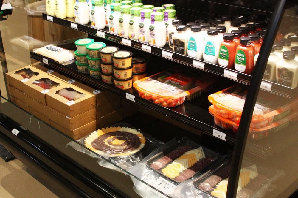Refrigerated store shelves stocked with various dressings, tubs of dip, packaged snacks, and deli items.